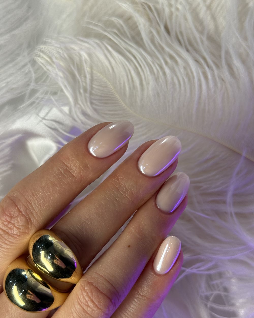 Nude nails with a gold ring on white feathers